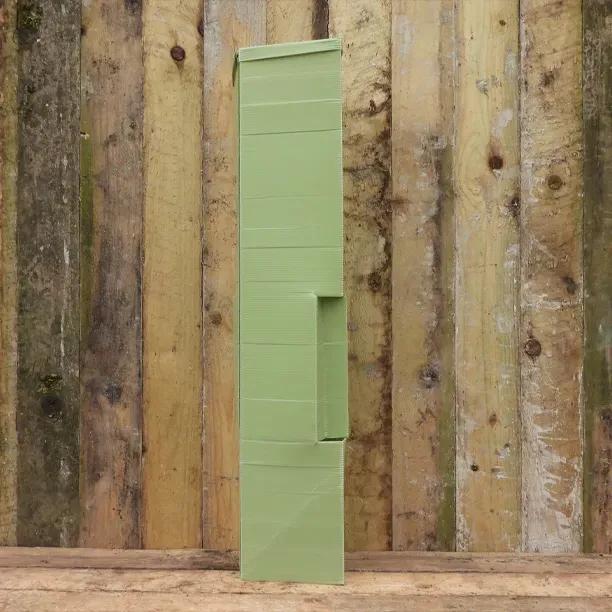 Defender Pro Tree Shelter green plastic tube guard standing against rustic wooden fence backdrop